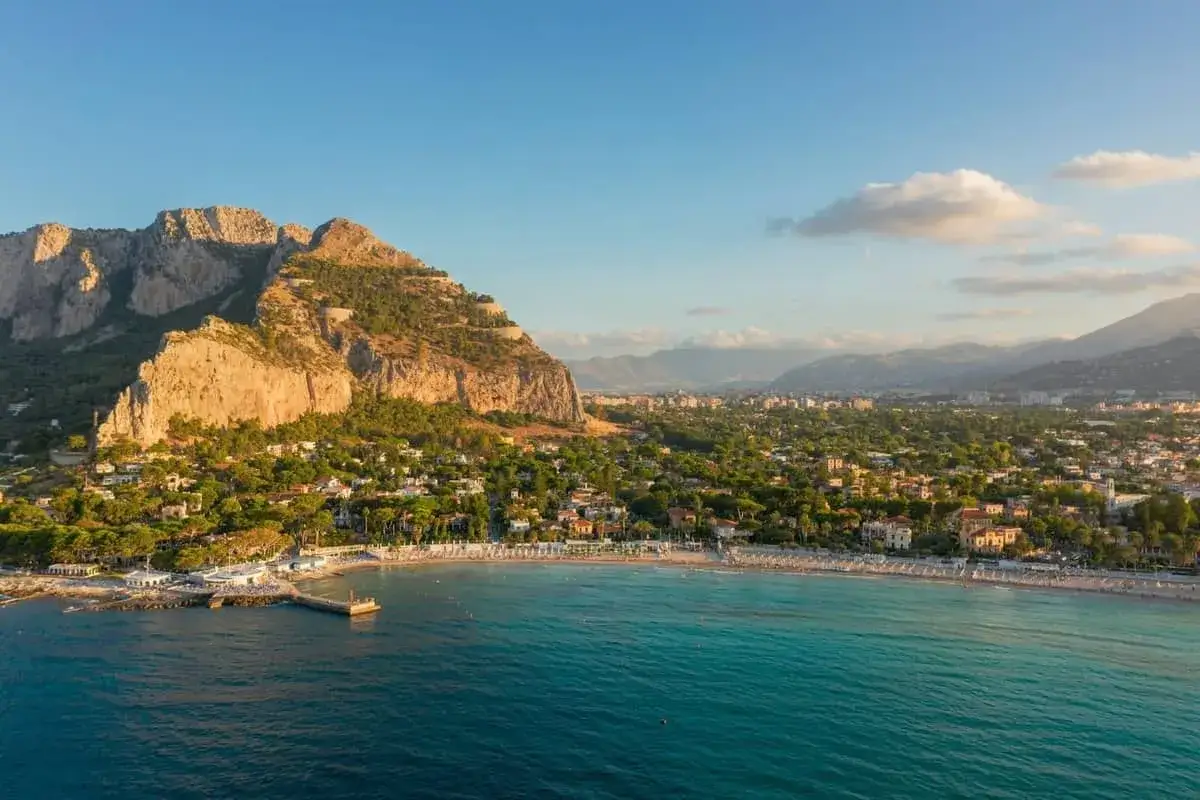 Malownicze Palermo plaża z turkusową wodą, skalistym masywem i zabudowaniami w tle.