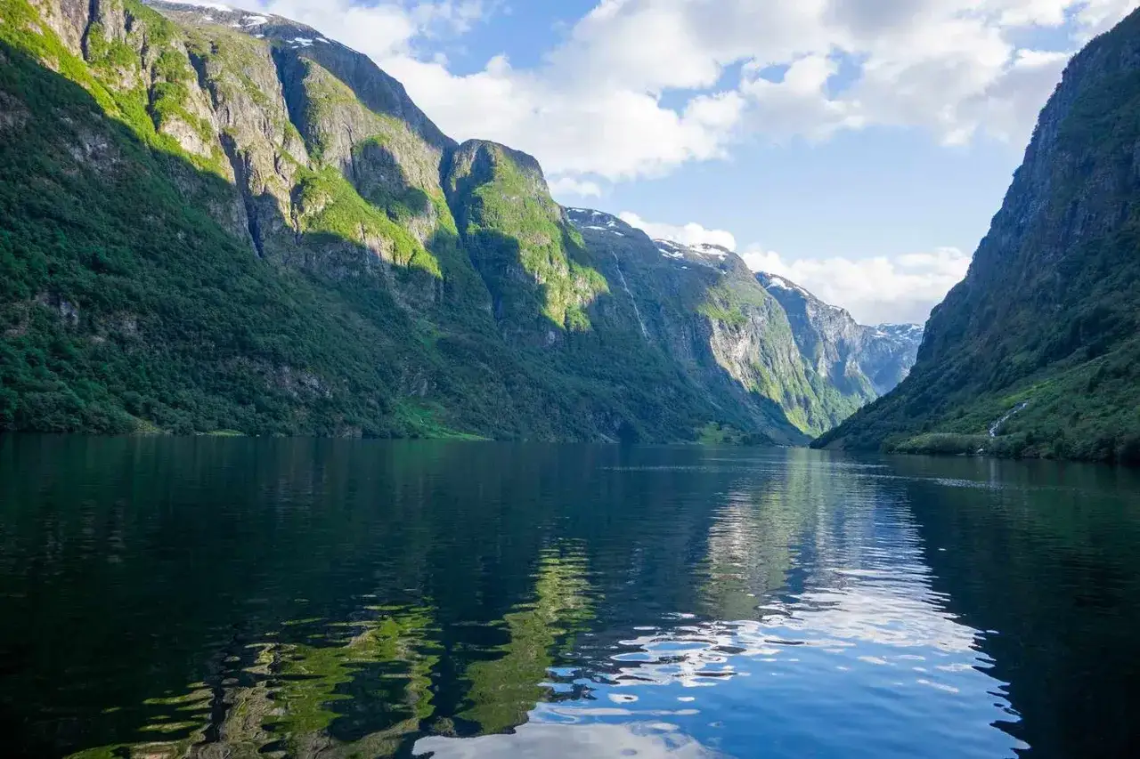 Majestatyczne, zielone góry otaczają spokojne wody, tworząc zapierający dech w piersiach widok na norweskie bergen fiordy.