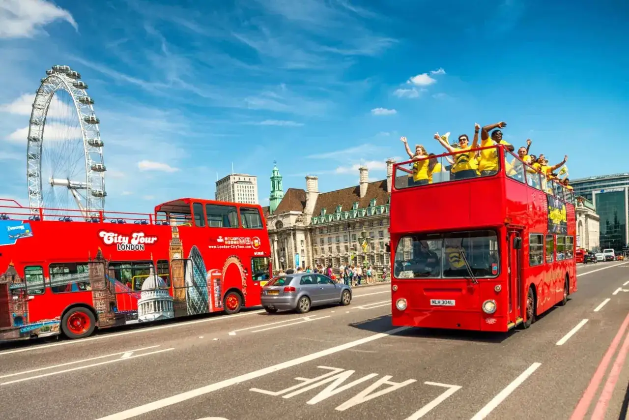 Dwa czerwone, piętrowe autobusy w Londynie, jeden z widokiem na London Eye, drugi z pasażerami na górnym pokładzie.