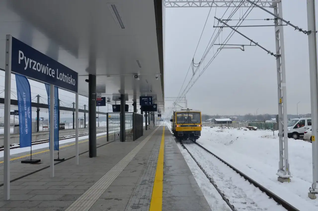 Żółty pociąg na stacji Pyrzowice Lotnisko w zimowej scenerii.