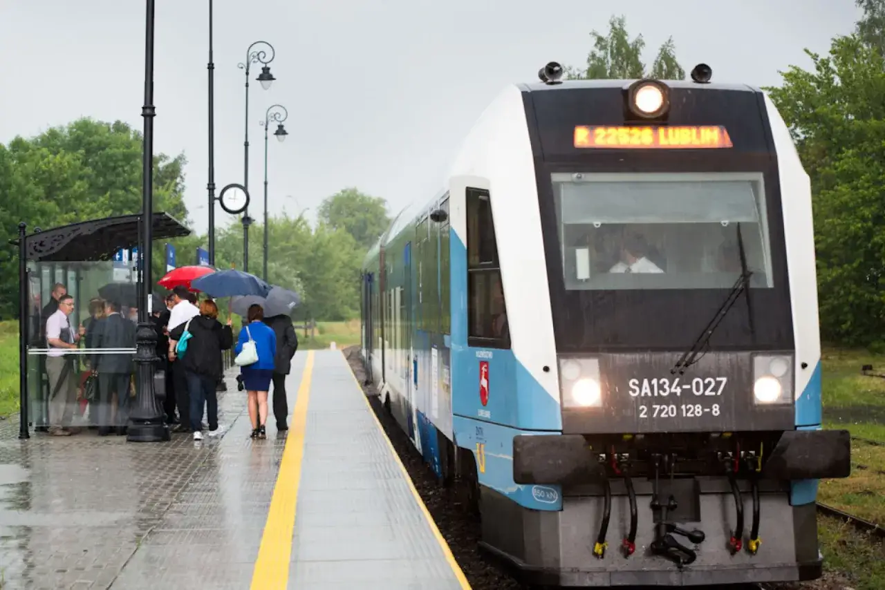 Szynobus Lublin - Zamość trasa. Pasażerowie z parasolami czekają na peronie na deszczowy dzień.
