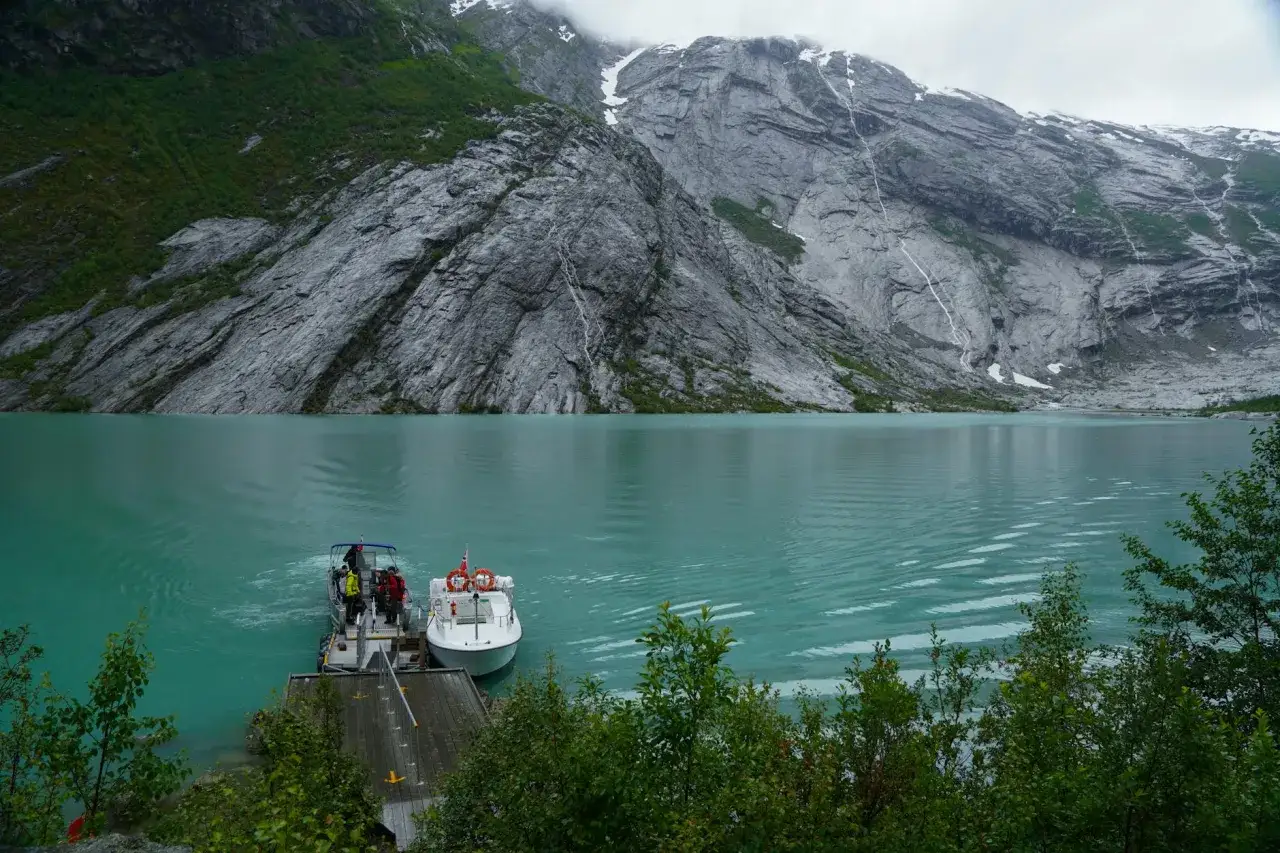Turkusowa woda i skaliste zbocza tworzą malowniczy fiord w Norwegii. Dwa statki czekają przy pomoście, gotowe na kolejną podróż.