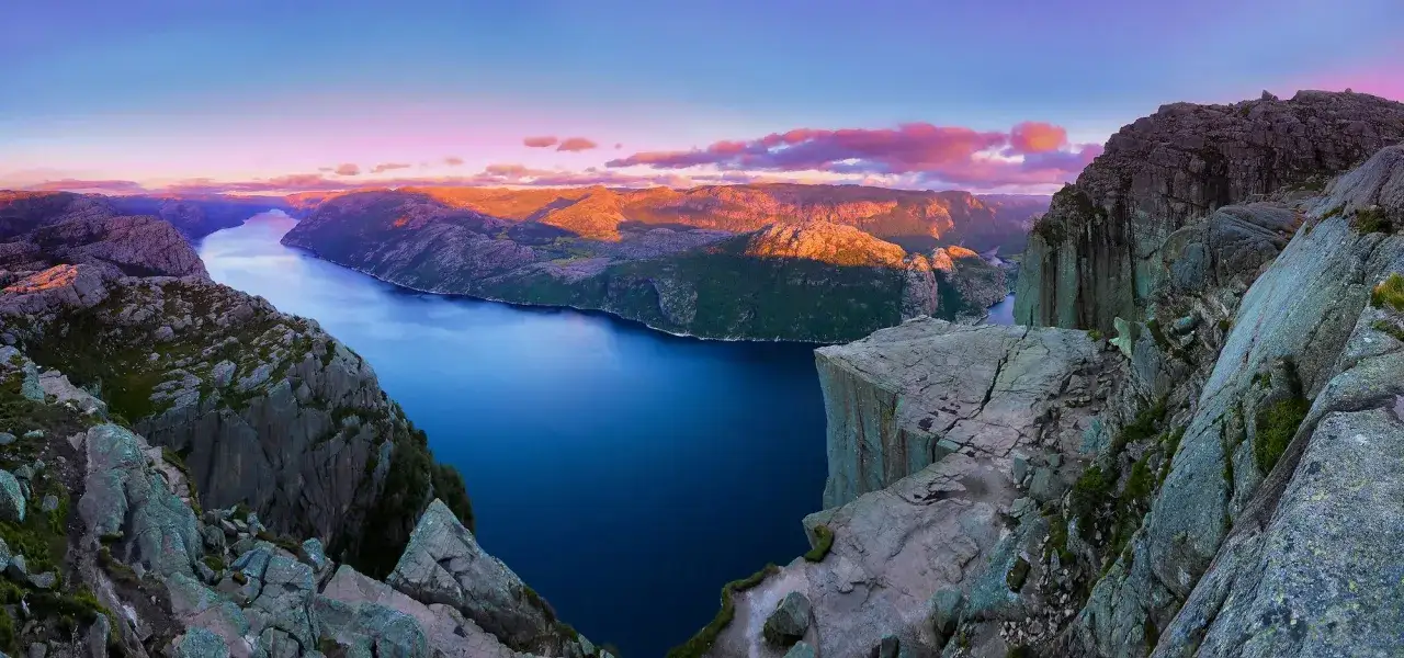 Zachód słońca nad Lysefjordem, jednym z najpiękniejszych fiordów w Norwegii. Skaliste zbocza i spokojna, błękitna woda tworzą zapierający dech w piersiach krajobraz.