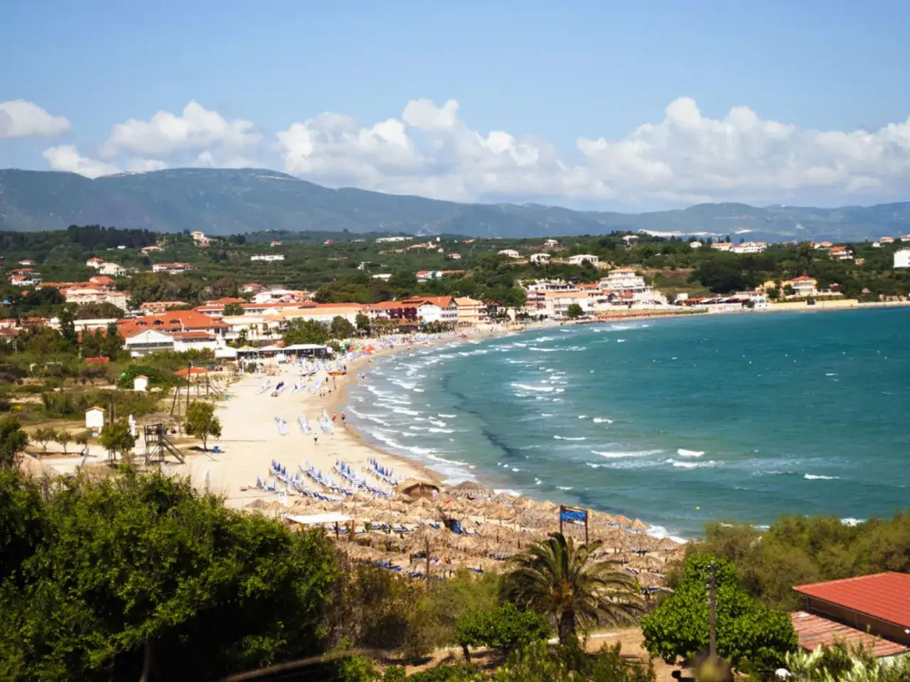 Piękna plaża w Tsilivi, z turkusową wodą, rzędami leżaków i parasoli, oraz zabudowaniami w tle.