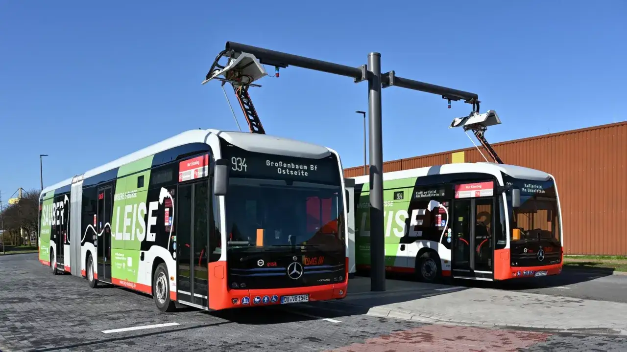 Dwa nowoczesne autobusy elektryczne podłączone do ładowania. Zielono-białe pojazdy z napisem 