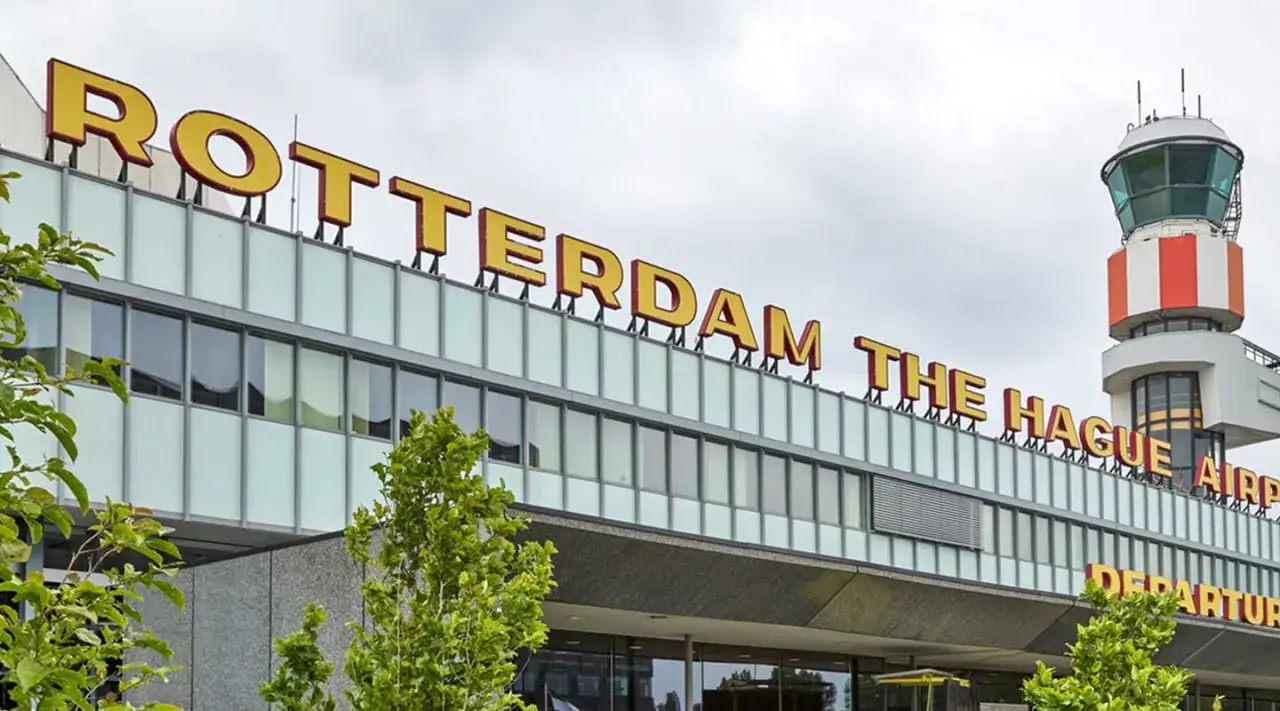 Rotterdam The Hague Airport, z charakterystyczną wieżą kontroli lotów i zielenią przed budynkiem.