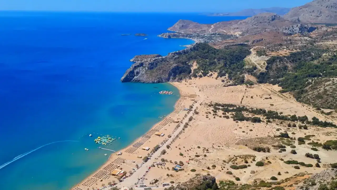 Malownicza plaża z leżakami i parasolami, wodny park rozrywki, turkusowe morze i skaliste wybrzeże w pobliżu Cathrin Hotel Rodos.
