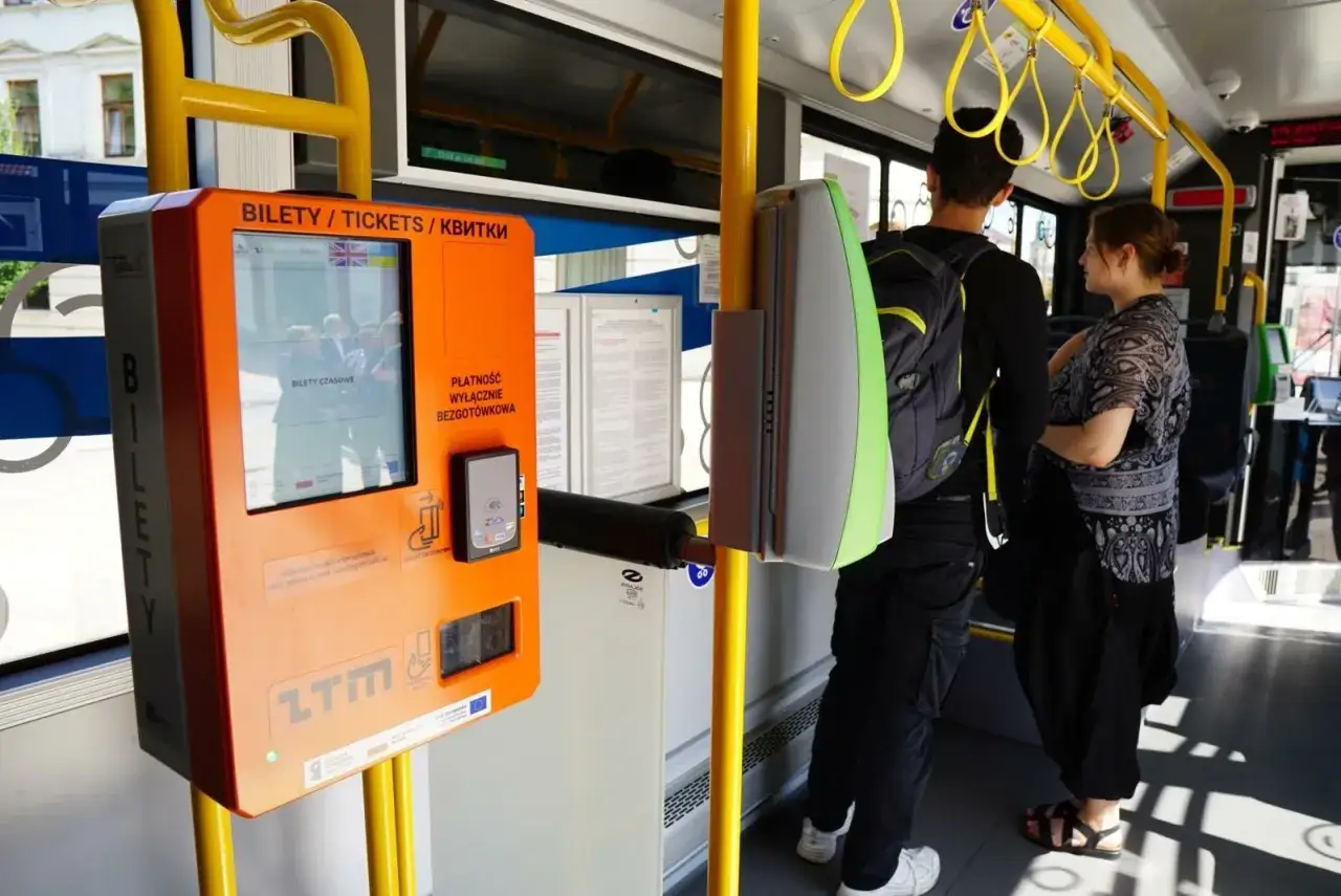 Bilet na autobus kupisz w automacie. Widoczni pasażerowie czekają na zakup.