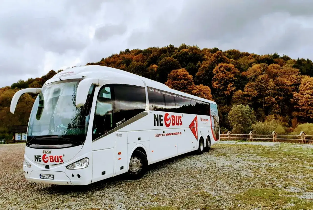 Biały autokar Neobus zaparkowany na tle jesiennego lasu. Sprawdź neobus ceny biletów na stronie www.neobus.pl.