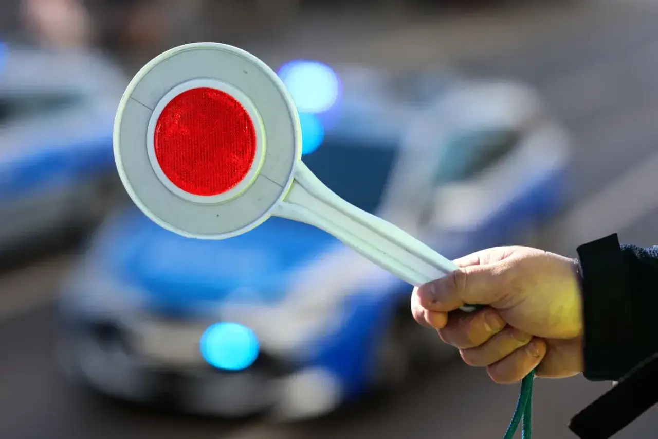 Ręka trzymająca znak stopu przed policyjnym radiowozem. Uważaj na mandaty w Norwegii, bo policja czuwa.