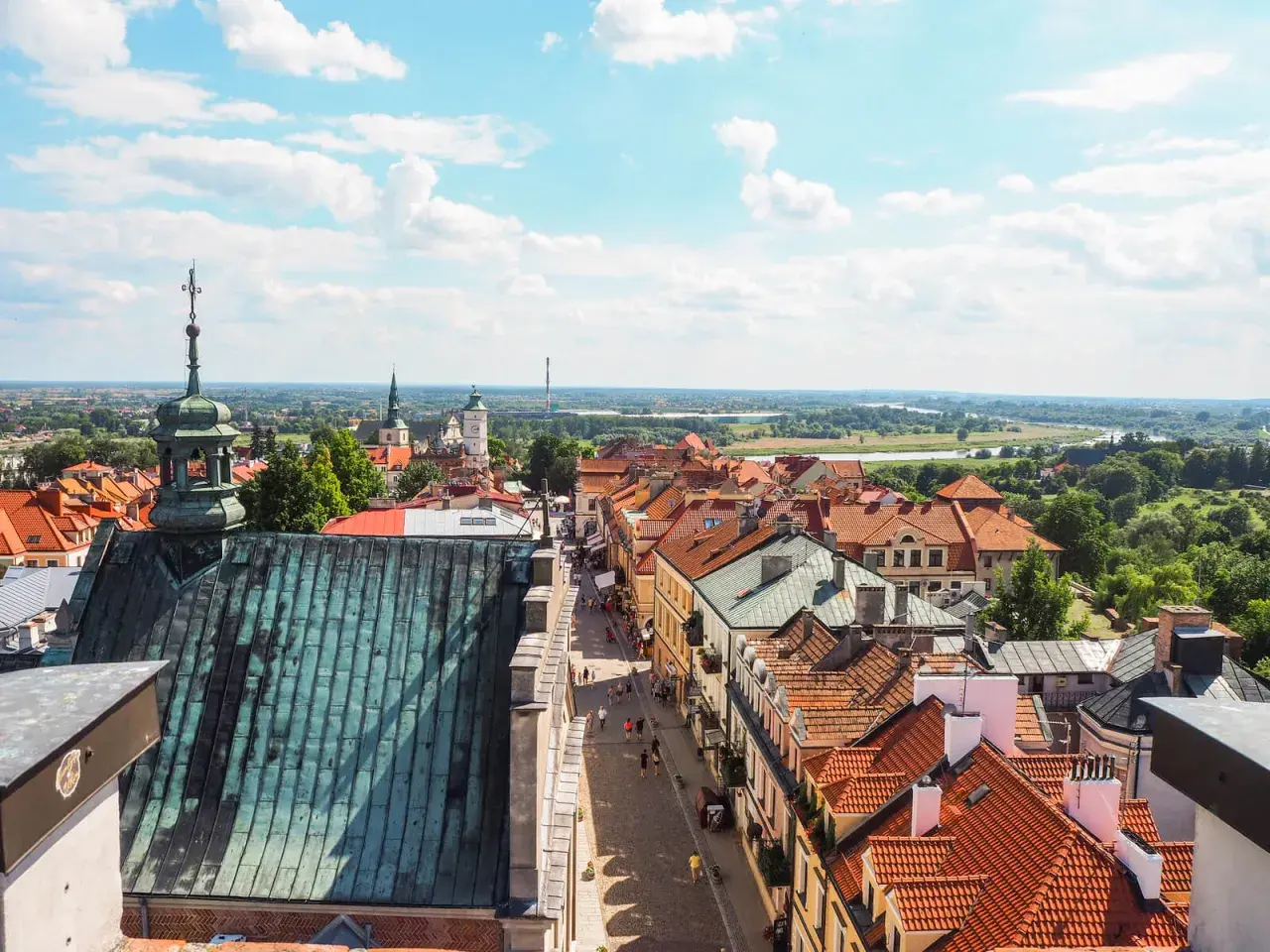 Widok na urokliwą sandomierz trasę z dachu kościoła. Czerwone dachy, wąska uliczka z ludźmi, a w tle rozległa panorama miasta i rzeki.